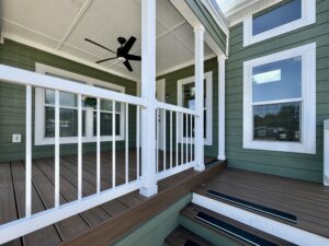 Green house exterior with white trim on Meandering Lane, wooden porch, black ceiling fan, and steps to the entrance.