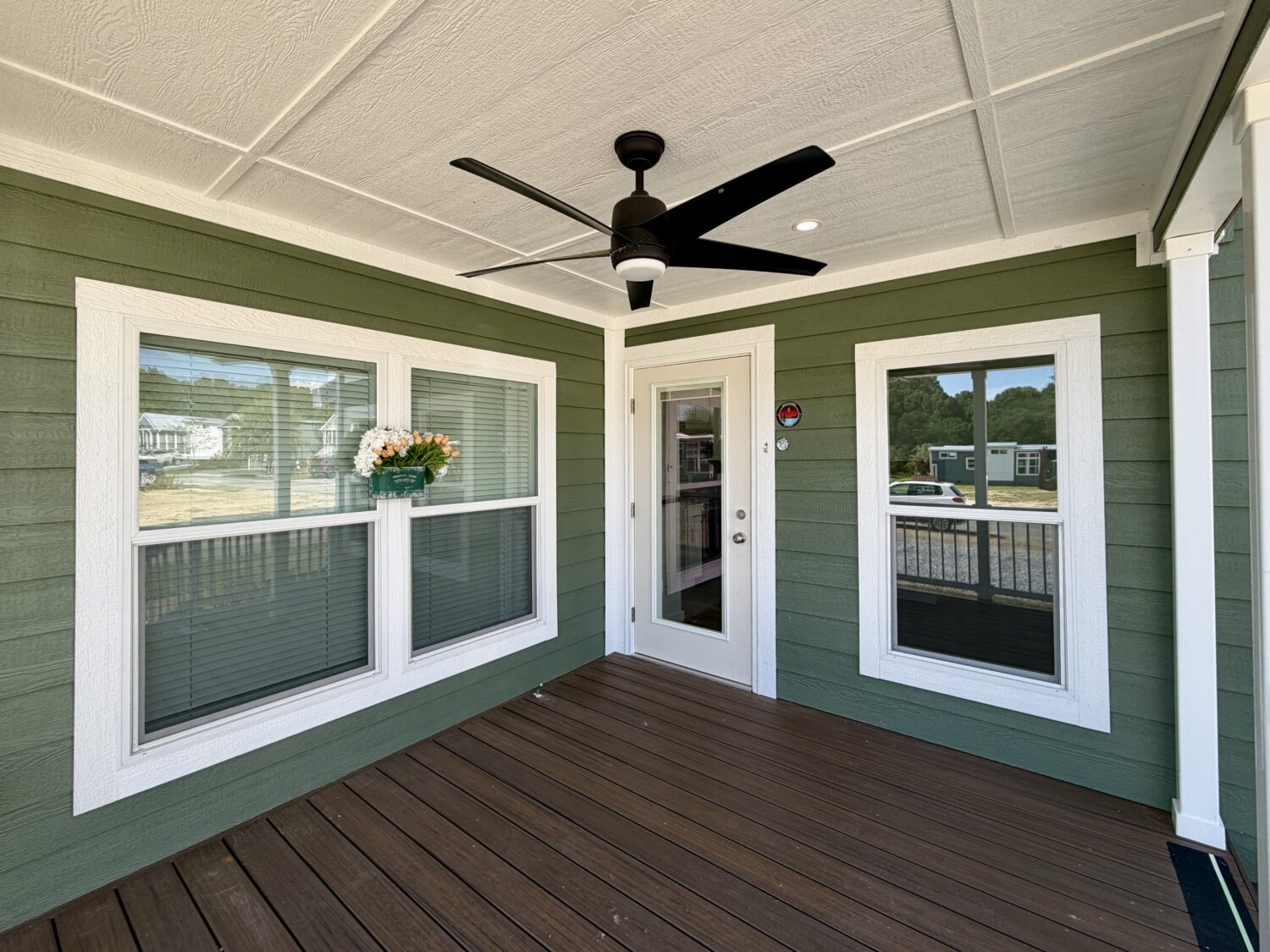 Green porch with white trim at 100 Meandering Lane, featuring a ceiling fan, flower box, and glass door on wood floor.