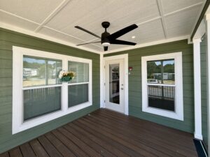 Green porch with white trim at 100 Meandering Lane, featuring a ceiling fan, flower box, and glass door on wood floor.