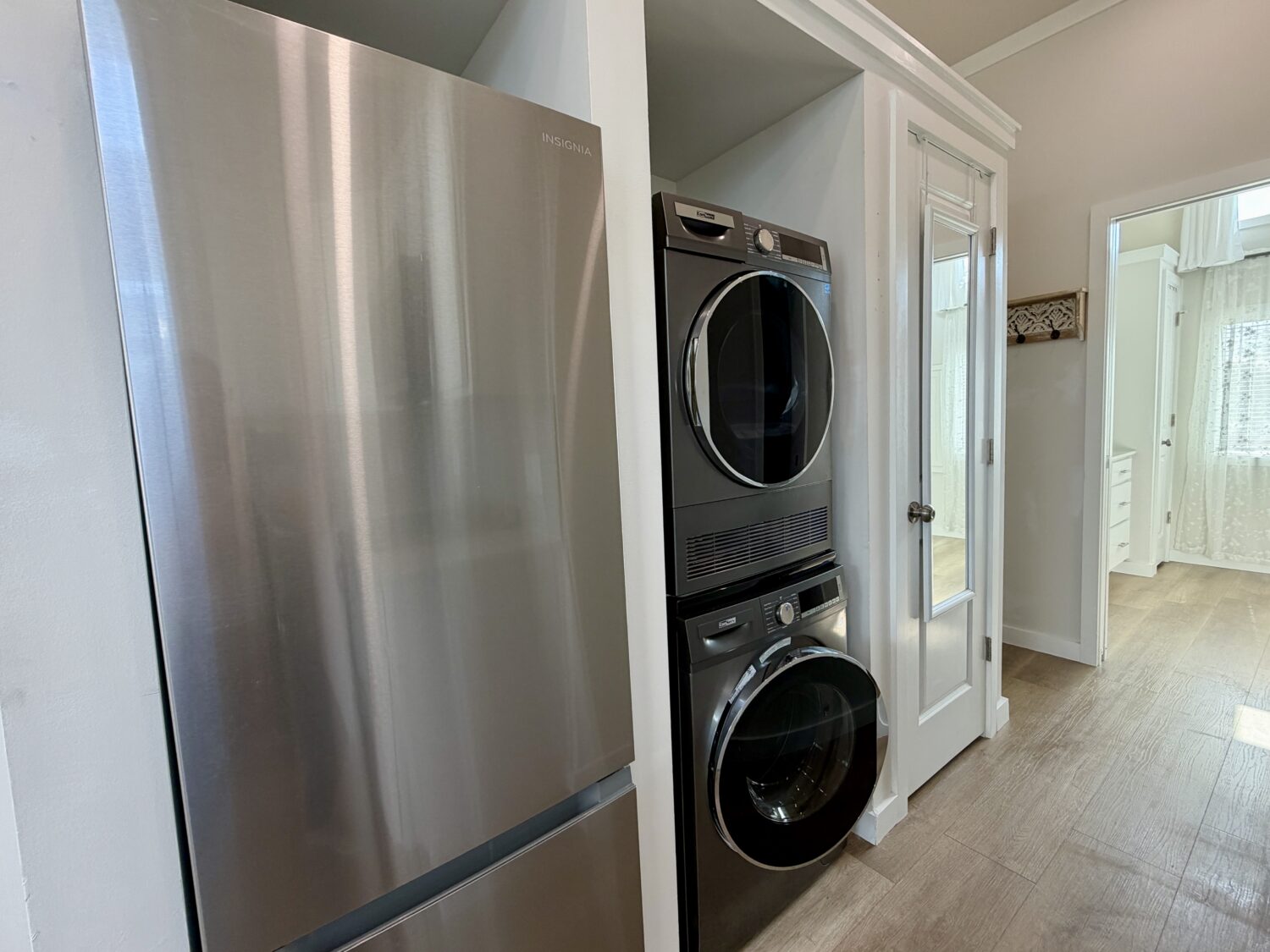 A stainless steel fridge and stacked washer and dryer sit beside a white door in this Meandering Lane modern laundry area.