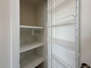 Empty pantry at 100 Meandering Lane with white shelves and metal wire baskets on the door, viewed from the entrance.