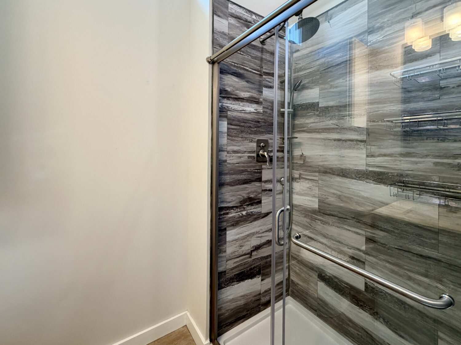 Glass shower with gray tile, metal grab bar, and wood floor peek—elegant design at 100 Meandering Lane.