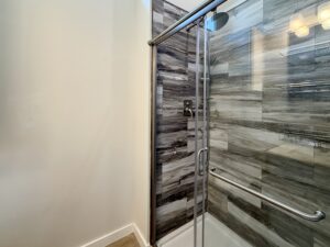 Glass shower with gray tile, metal grab bar, and wood floor peek—elegant design at 100 Meandering Lane.