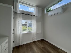 Bright room at 100 Meandering Lane with wood floors, white walls, two windows, sheer curtains, and AC.