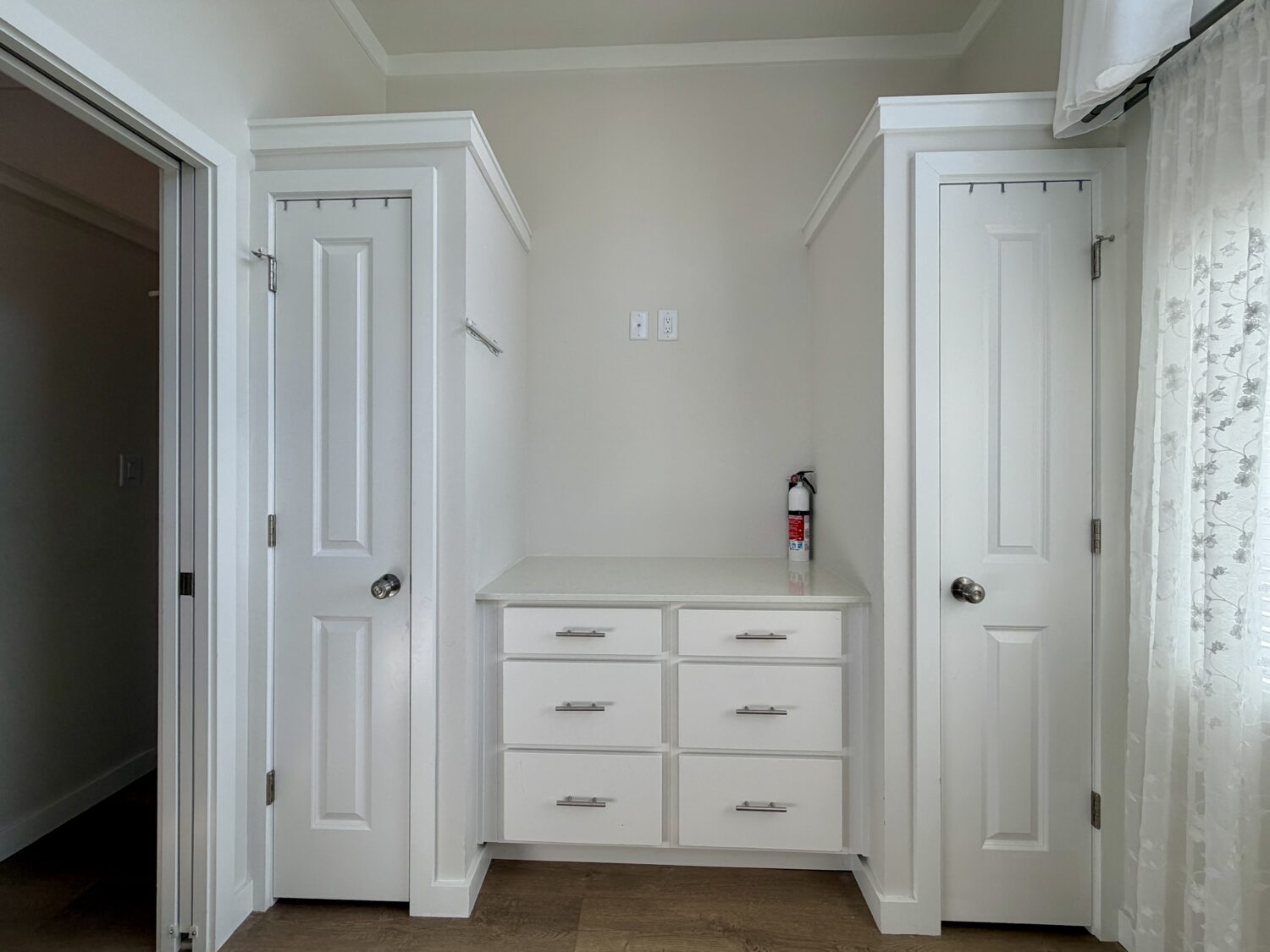 Two white doors flank six drawers with a fire extinguisher atop, set against a beige wall on Meandering Lane.