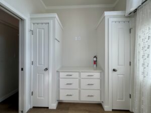 Two white doors flank six drawers with a fire extinguisher atop, set against a beige wall on Meandering Lane.