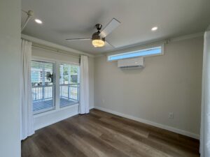 Bright empty room at 100 Meandering Lane with wood floors, ceiling fan, window blinds, curtains, and wall AC.