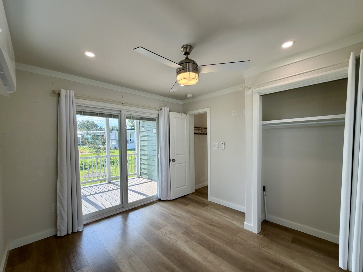 Bright empty bedroom at 100 Meandering Lane with wood floors, ceiling fan, open closet, and deck with green view.