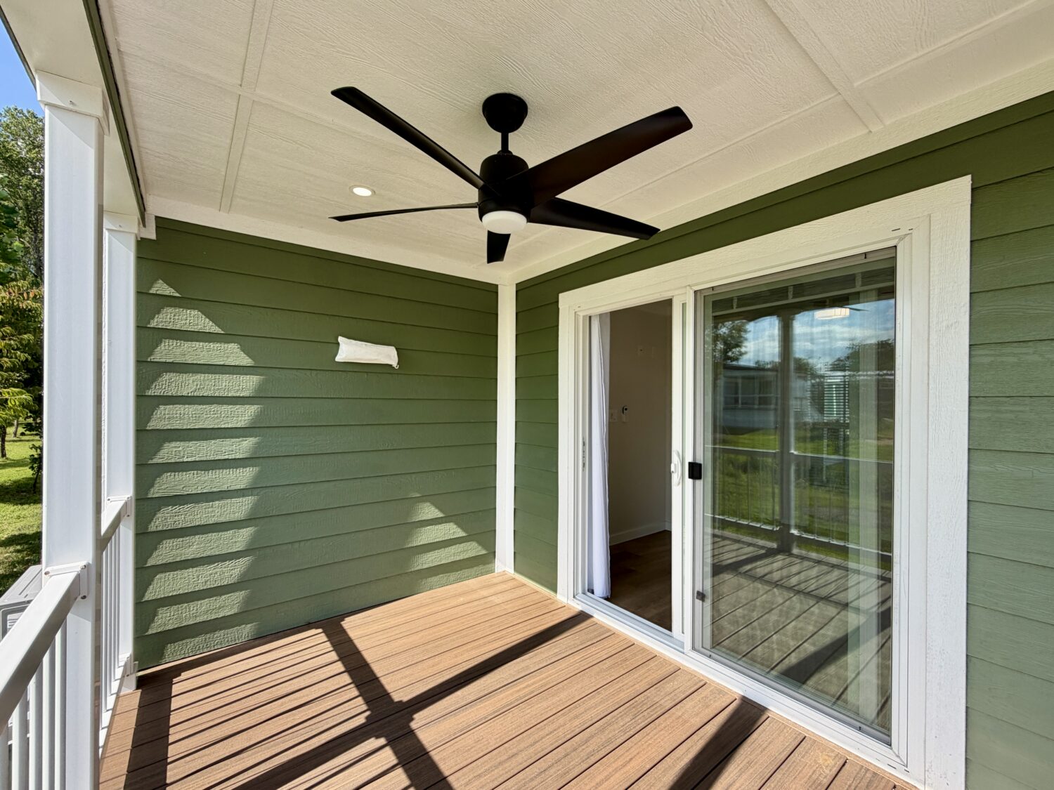 Small green porch with wood flooring on Meandering Lane, a black ceiling fan, and a glass sliding door leading inside.