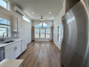 Bright kitchen and living area at 100 Meandering Lane, with large windows, white cabinets, wood floors, and stainless steel.