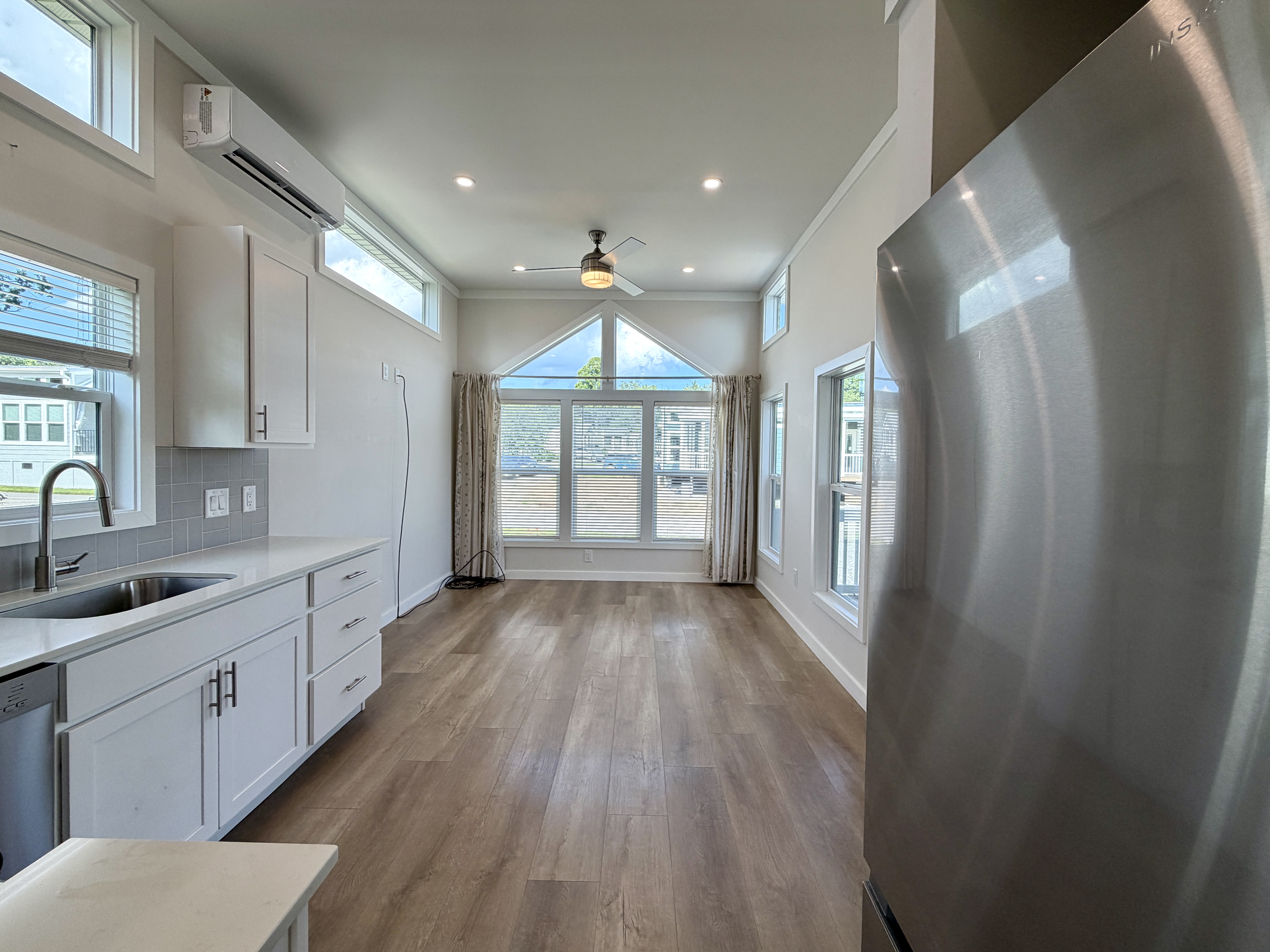 Bright kitchen and living area at 100 Meandering Lane, with large windows, white cabinets, wood floors, and stainless steel.