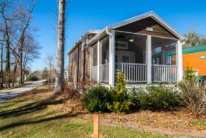 A small brown house with a screened porch sits at 66 Empire Lane, surrounded by trees and shrubs under a blue sky.