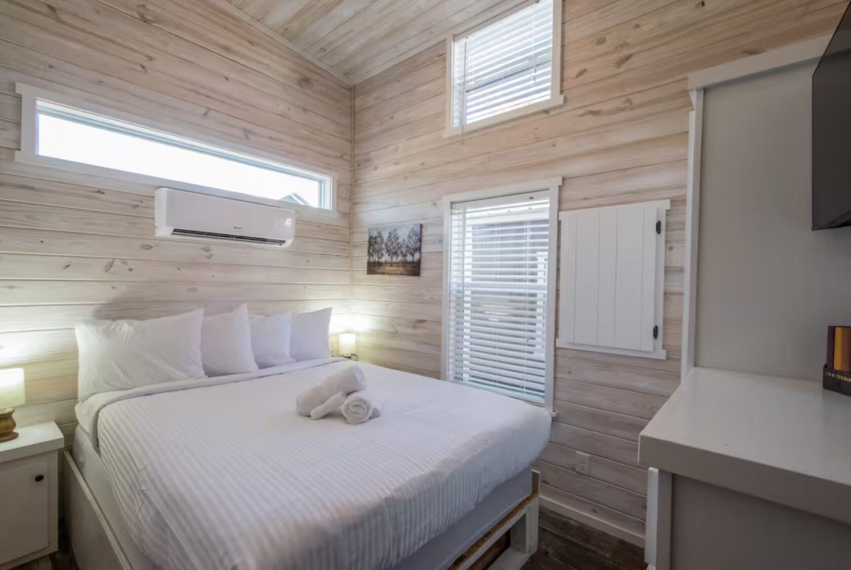 Cozy bedroom at 66 Empire Lane with a neatly made bed, white linens, wooden walls, lamps, and natural light.