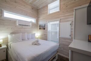 Cozy bedroom at 66 Empire Lane with a neatly made bed, white linens, wooden walls, lamps, and natural light.