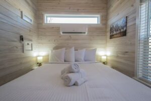 A neatly made bed with white linens and folded towels in a wood-paneled room at 66 Empire Lane, with window and wall art.
