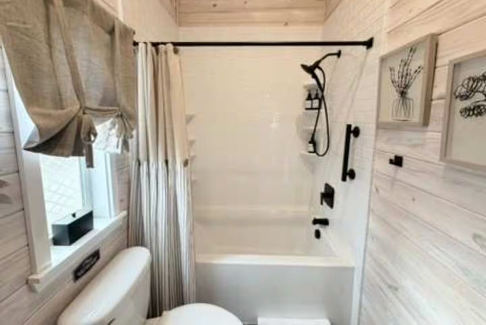 Charming small bathroom at 66 Empire Lane features a tub, shower curtain, window, light wood walls, and framed art.
