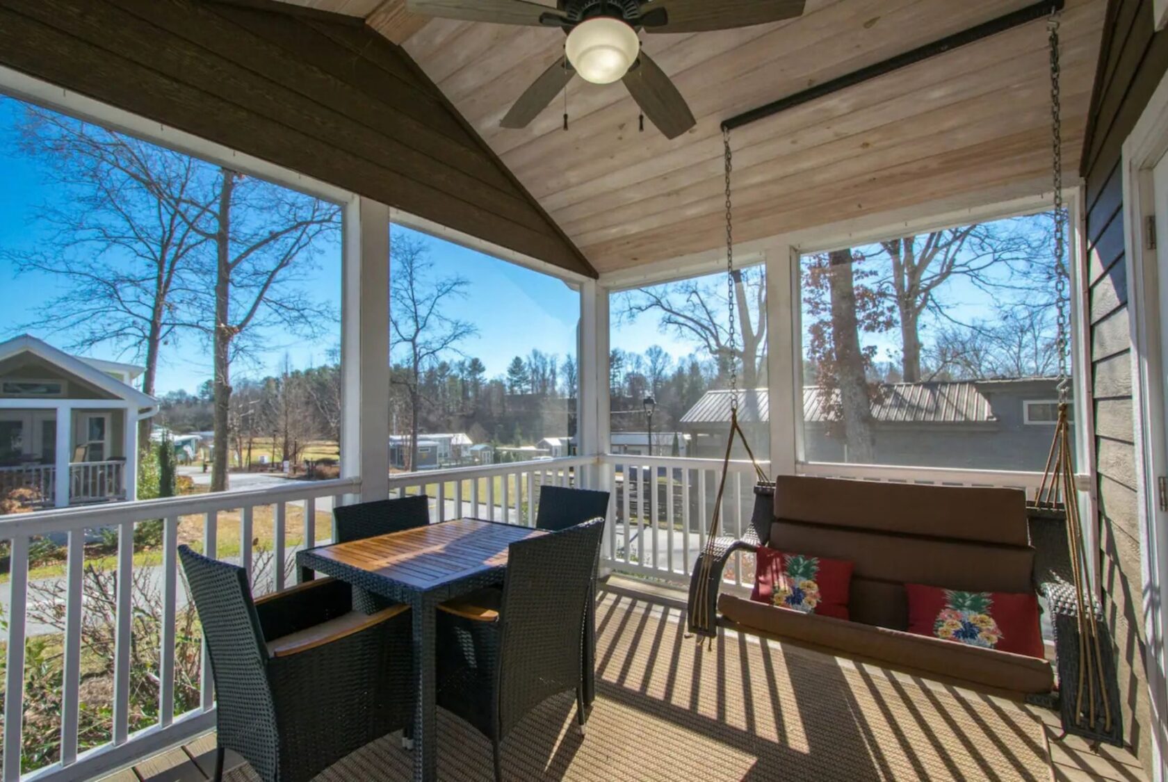 66 Empire Lane features a screened porch with a ceiling fan, wicker dining set, and swing bench overlooking a sunny yard.