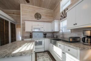 Modern kitchen at 66 Empire Lane with white cabinets, marble counters, farmhouse sink, and sunlit wood walls.
