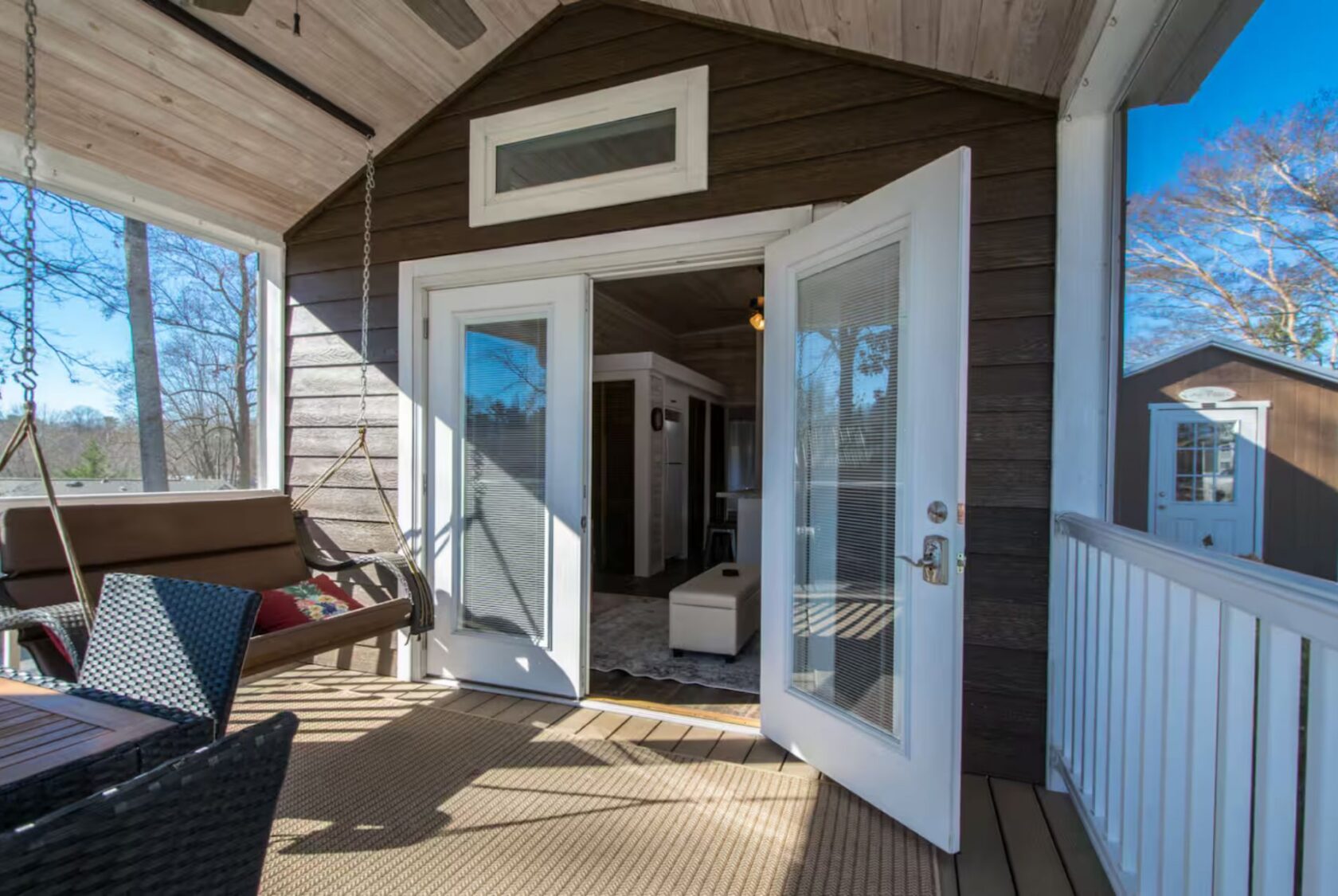 Open double doors at 66 Empire Lane lead from a sunlit porch with a swing into a cozy, modern cabin-style interior.